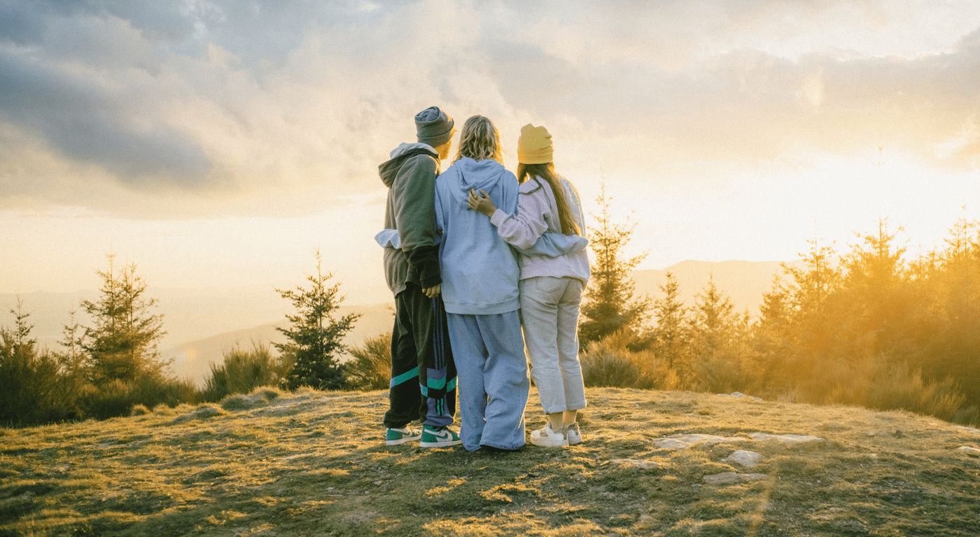 Tres jóvenes disfrutando de una puesta de sol en el bosque, acompañados de las mejores canciones para viajar.