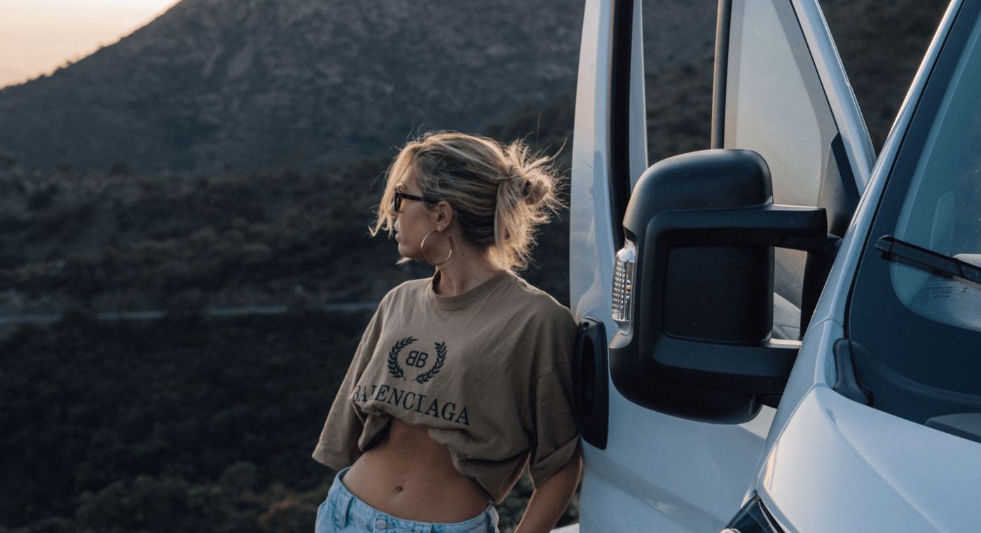 Chica disfrutando de un paisaje montañoso, apoyada en una camper Neo de Nomade Nation, perfecta para viajar en verano con libertad.