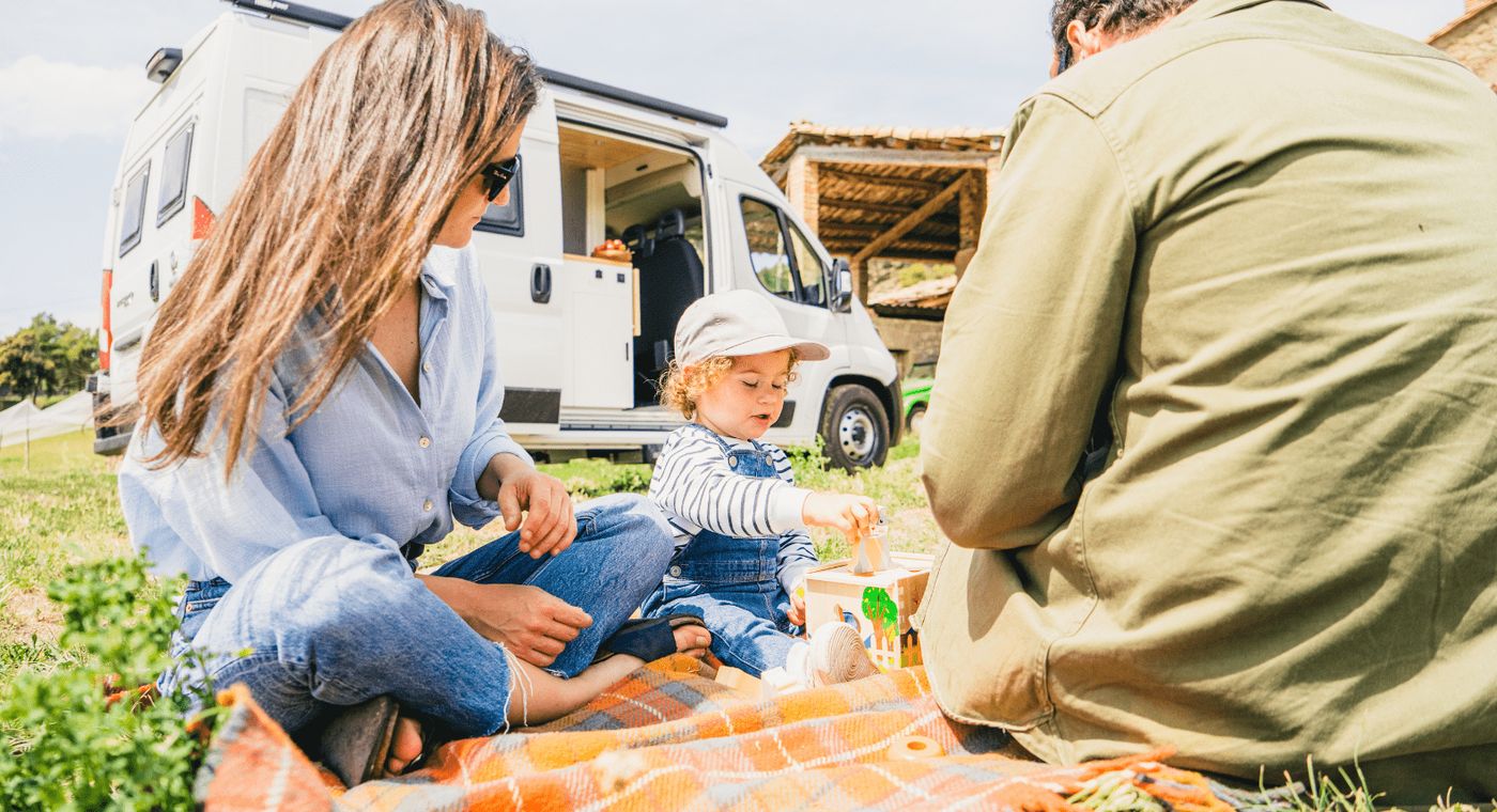 Familia con su bebé disfrutando del ecoturismo con su camper de fondo.