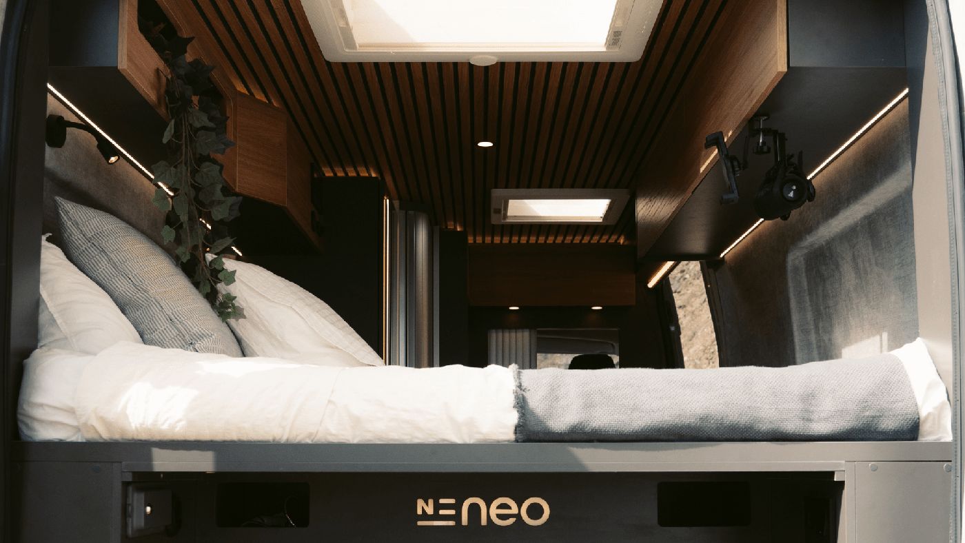 Dormitorio con cama doble en la furgoneta camper Neo, diseñado para descansar cómodamente en tus viajes.