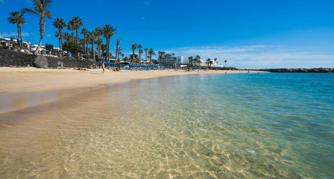 Playa Flamingo en Lanzarote con su arena blanca y aguas tranquilas, ideal para familias y un baño relajante.