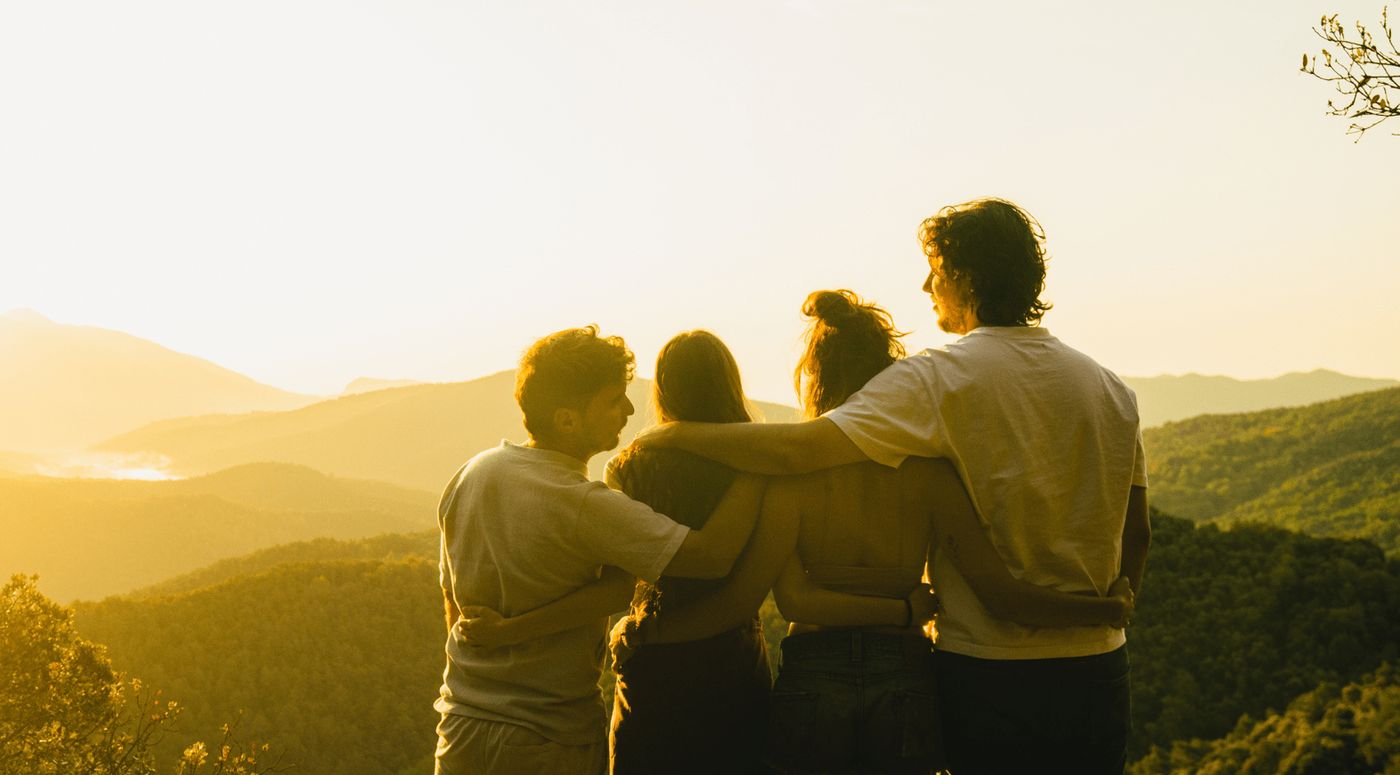 Grupo de amigos abrazados en un paisaje montañoso al atardecer durante su ruta.