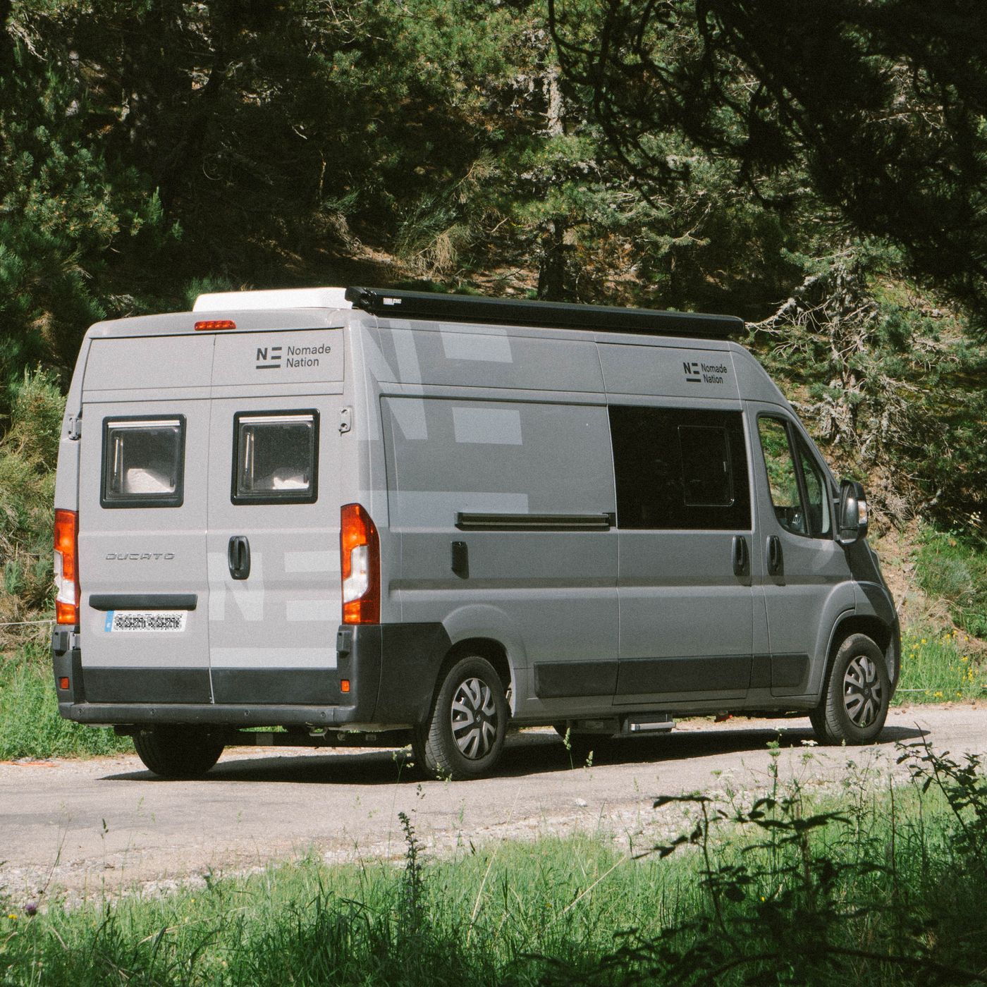 Furgoneta camper Neo circulando por una carretera rodeada de árboles, ideal para explorar nuevos destinos.