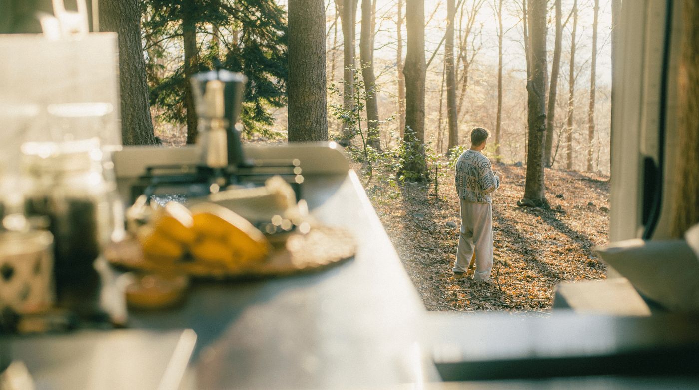 Vista desde el interior de una camper, con una persona contemplando el paisaje del bosque.