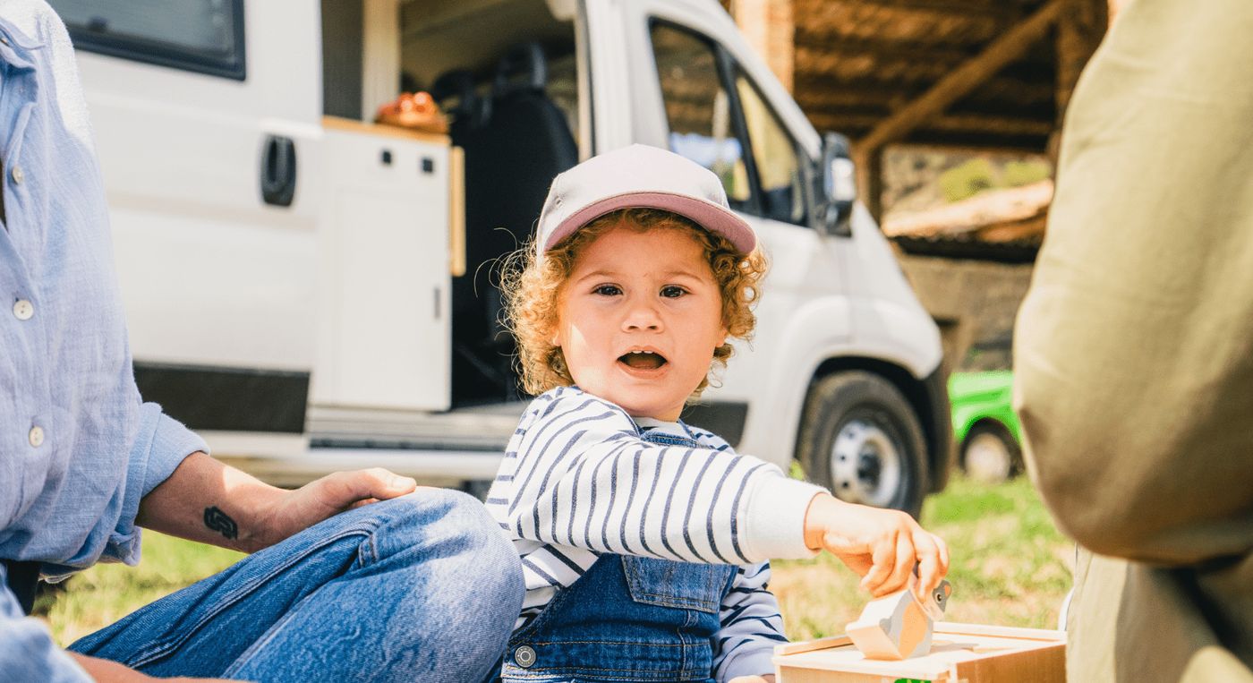Bebé jugando feliz en el exterior con una furgoneta camper de Nomade Nation de fondo, reflejando la experiencia de viajar en furgoneta camper con niños.