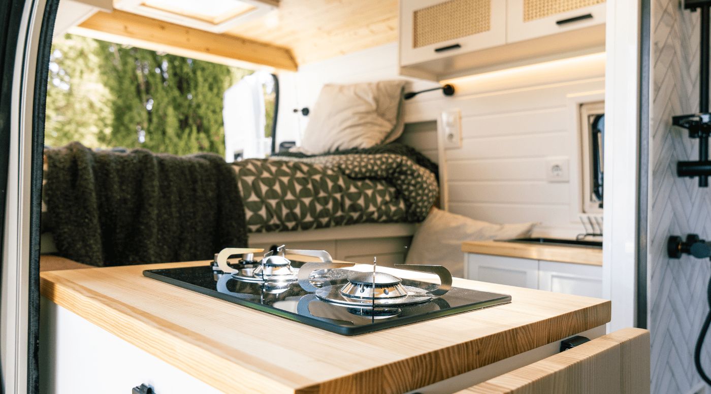 Cocina de dos fuegos de una furgoneta camper de Nomade Nation, con la cama y el baño al fondo.