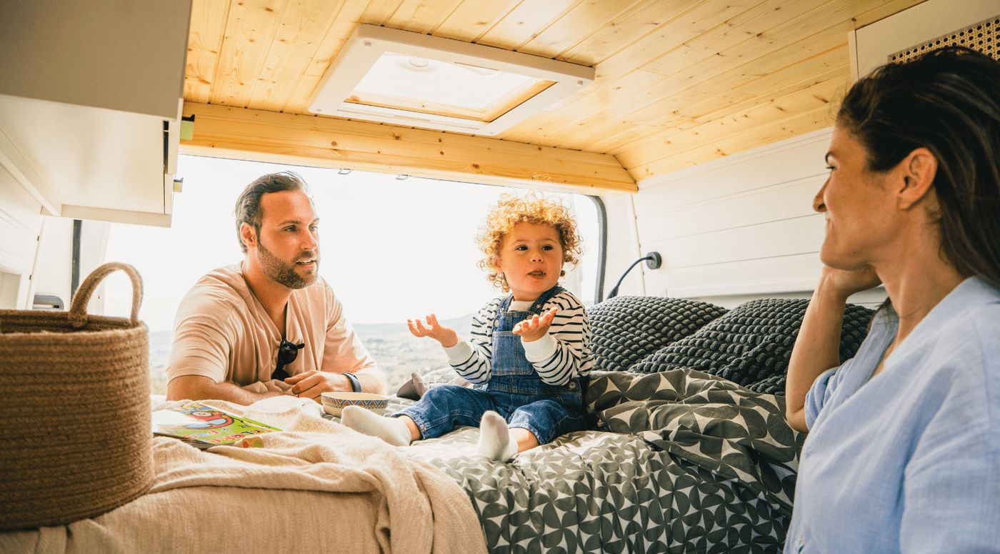 Familia con un niño pequeño en el interior de una furgoneta camper de Nomade Nation, con la puerta trasera abierta al paisaje.