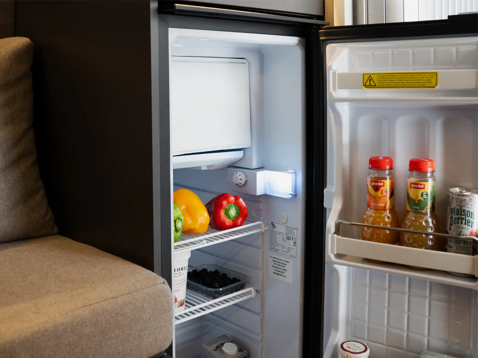 The fridge open beside the sofa, with food and drinks inside